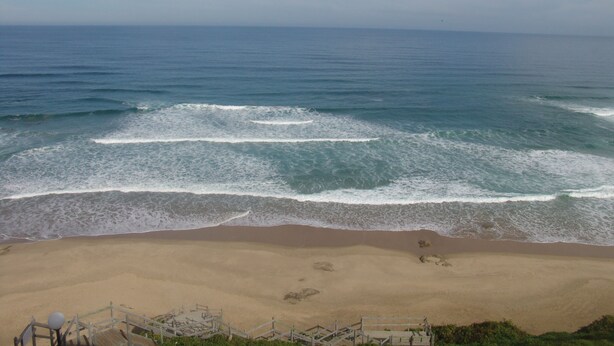 Una playa con olas, una orilla arenosa y una escalera de madera que baja a la playa.