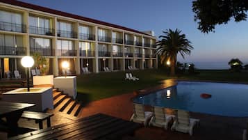 A hotel with a pool, outdoor seating, and a view of the ocean.