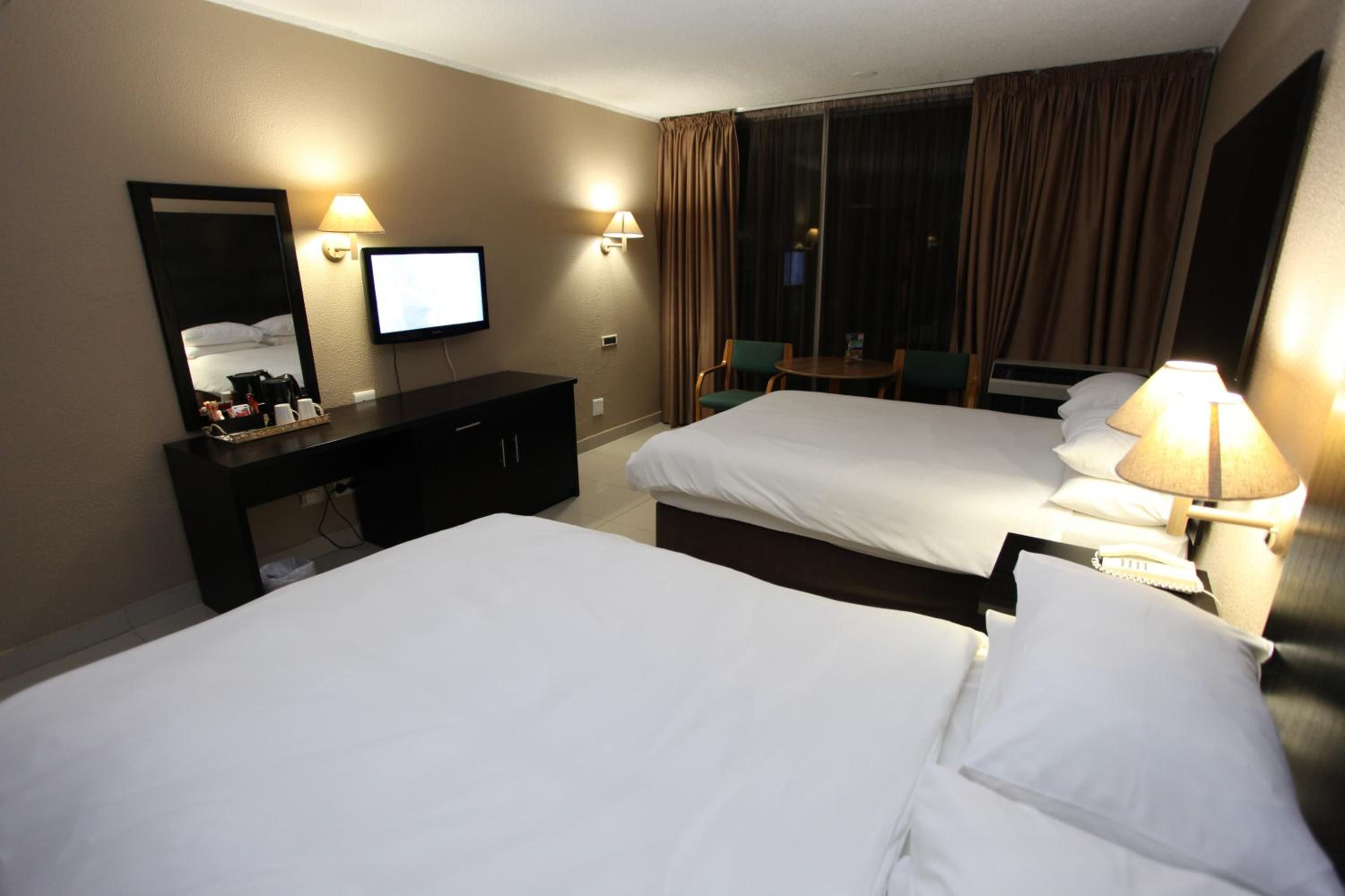 A hotel room with two beds, a TV, a desk, and a window with curtains.