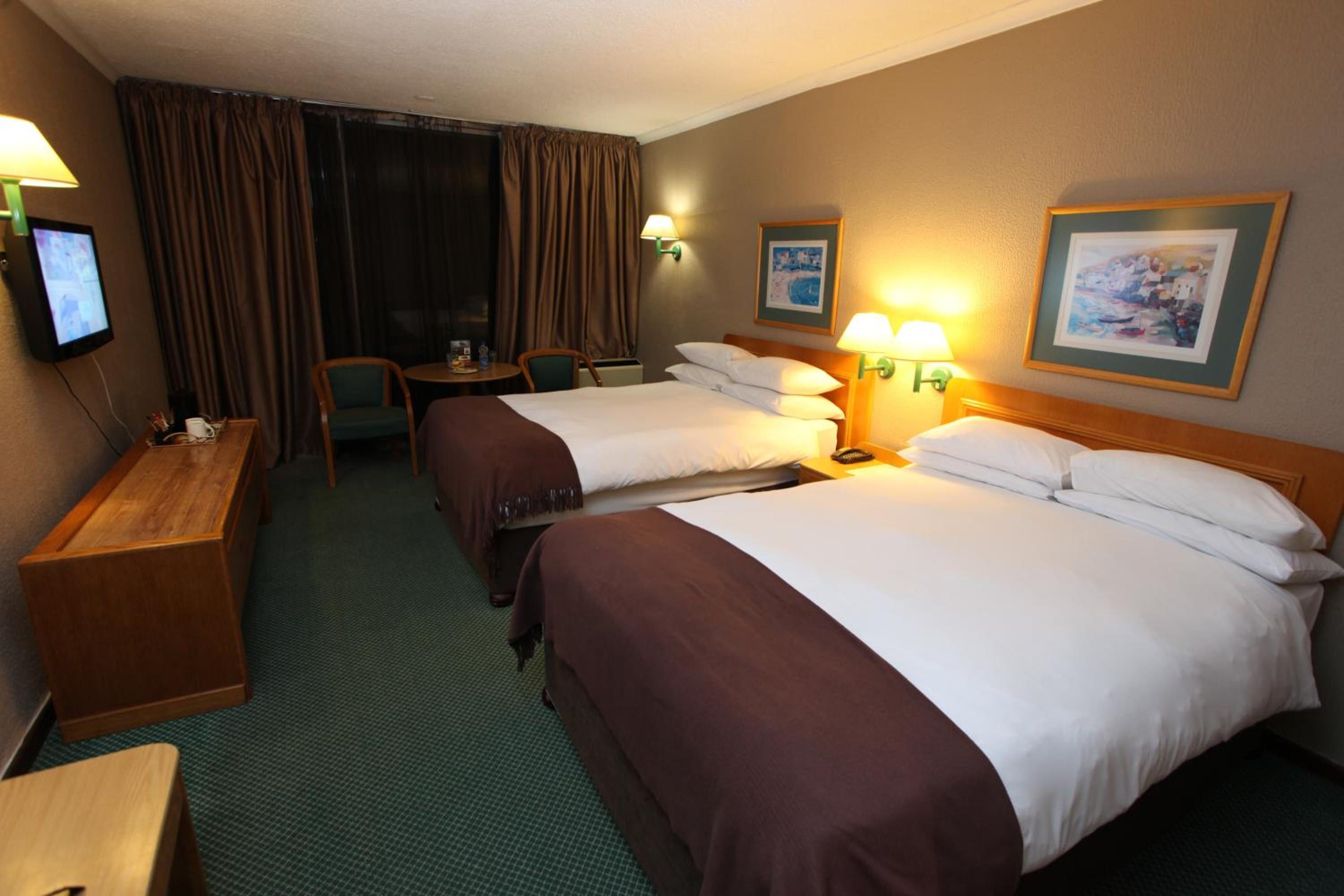 A hotel room with two beds, a desk, a chair, a television, and two wall-mounted lamps.