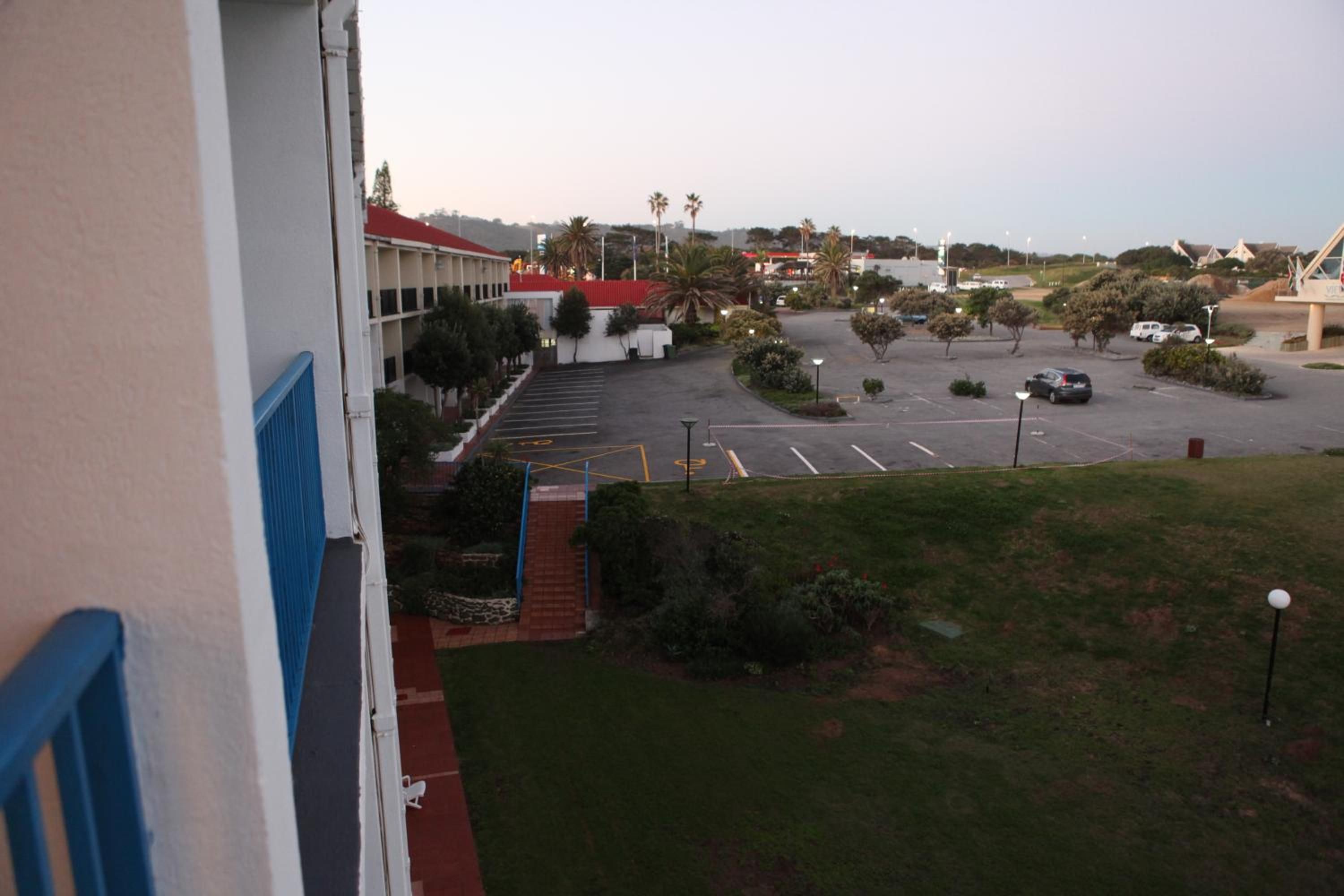 A parking lot with multiple cars, a building with a red roof, and a grassy area with trees.