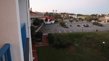 A parking lot with multiple cars, a building with a red roof, and a grassy area with trees.