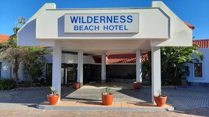 Entrada del Wilderness Beach Hotel con un porche cubierto, plantas en macetas y un cielo azul despejado.