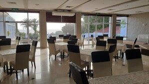Un amplio comedor interior con varias mesas y sillas, grandes ventanales que ofrecen vistas al exterior y un equipo de aire acondicionado en el techo.