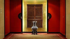 A hallway with a red and gold color scheme, a decorative vase on a pedestal, and a traditional door with intricate designs. - Gloria Prince Hotel Taipei (Taipei)
