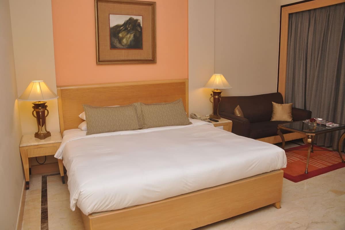 A hotel room with a large bed, two bedside tables with lamps, a sofa, a small table, and a painting on the wall.