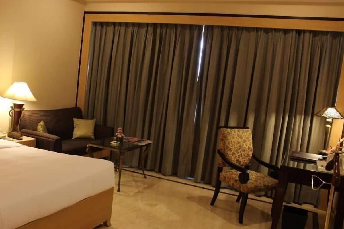 A hotel room with a bed, a desk, a chair, a table, and a large window with curtains.
