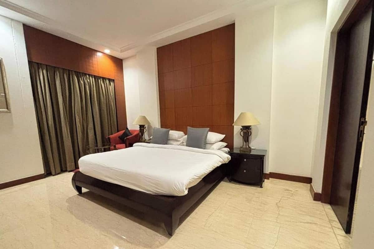 A modern hotel room with a large bed, two bedside tables with lamps, a wooden headboard, and a large window with curtains.