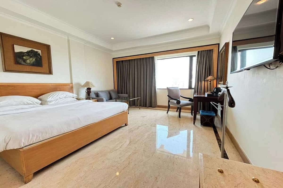 A hotel room with a large bed, a desk, a chair, a TV, and a window with curtains.