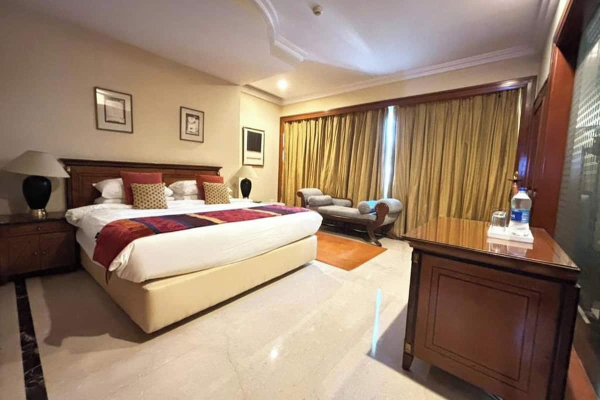 A hotel room with a large bed, a desk, a chair, a sofa, and a large window with curtains.