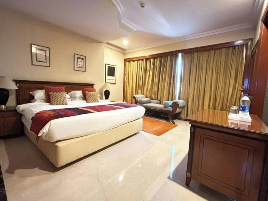 A hotel room with a large bed, a desk, a chair, a sofa, and a large window with curtains.
