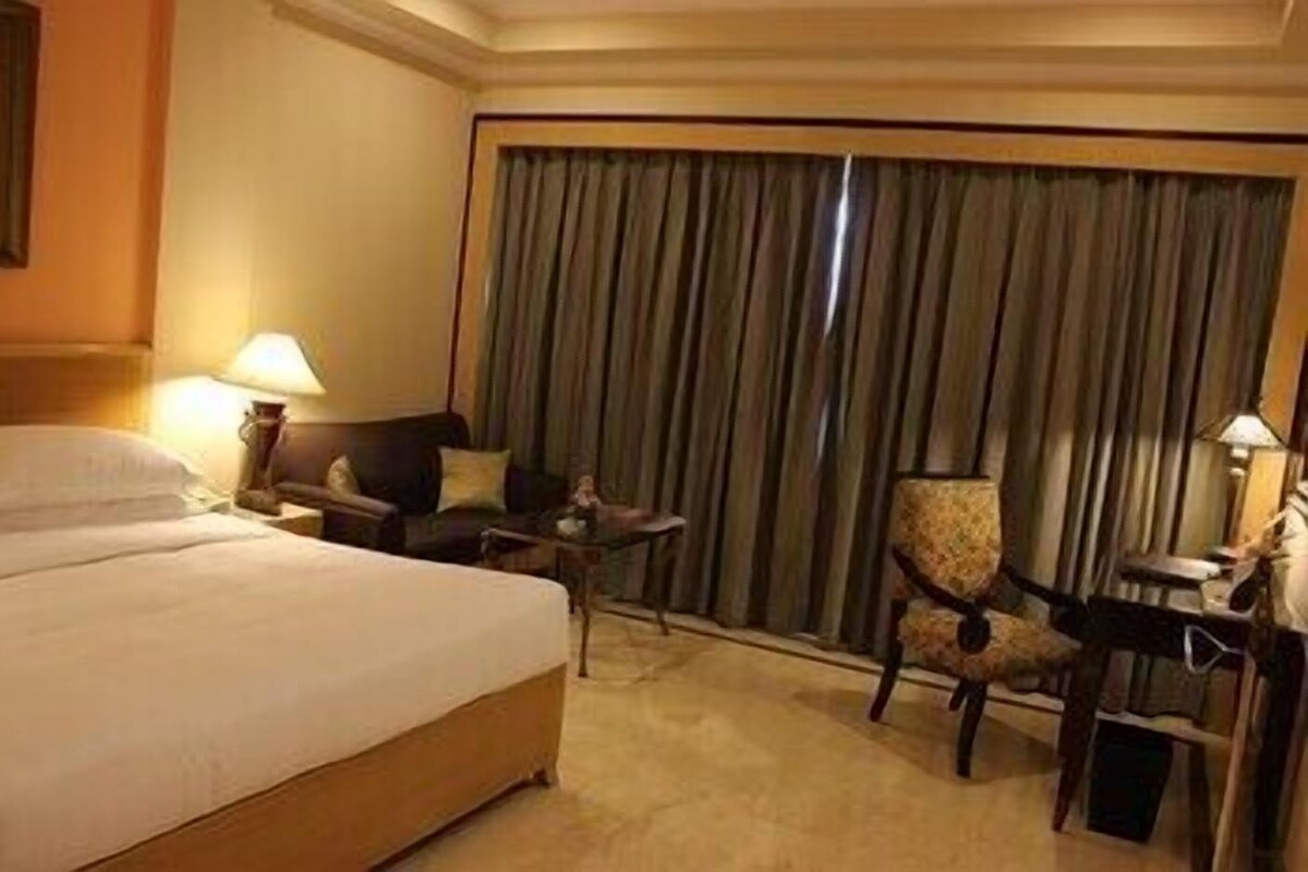 A hotel room with a bed, a desk, a chair, and a large window with curtains.