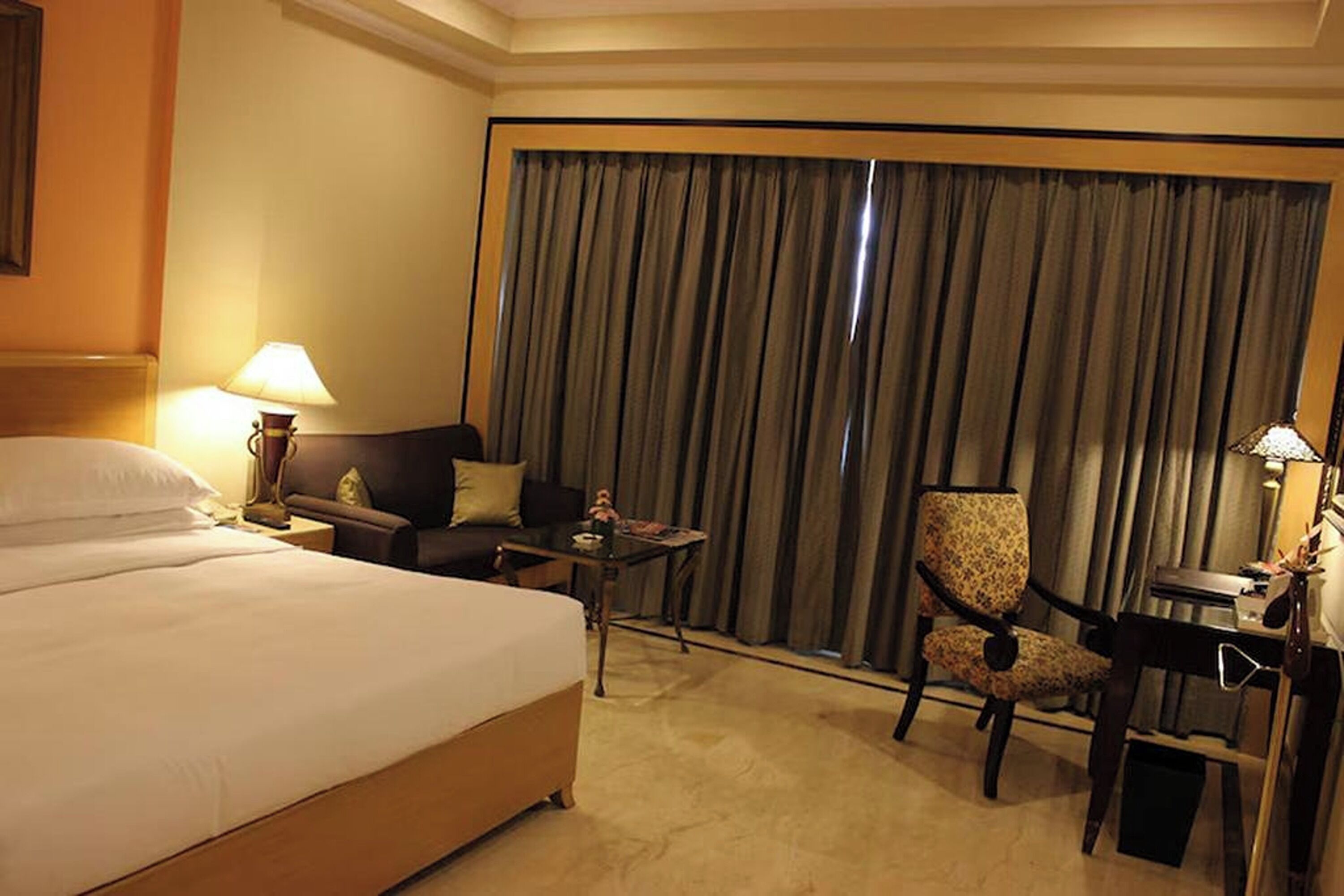 Una habitación de hotel con una cama grande, un escritorio, una silla y un ventanal con cortinas.