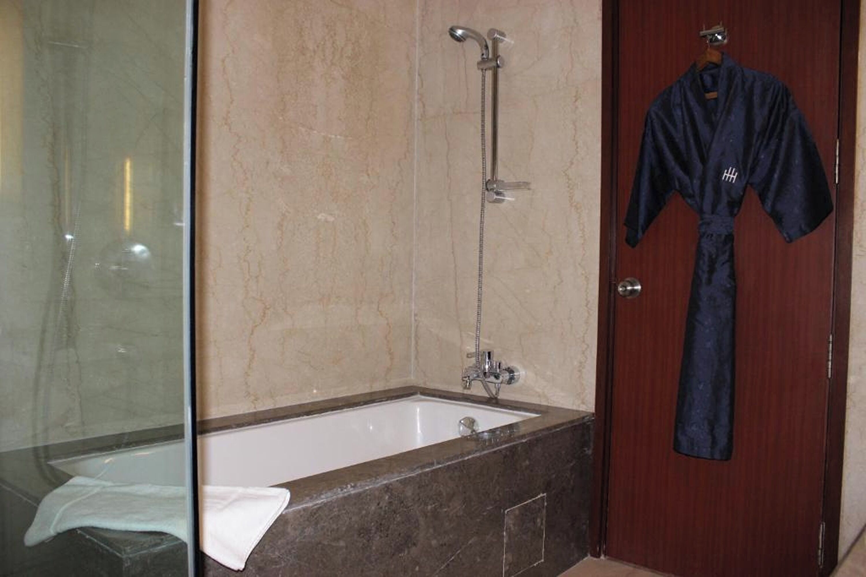 Une salle de bain avec une baignoire, un espace de douche en verre et une porte en bois sur laquelle est accroché un peignoir.