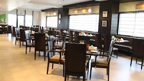 A spacious restaurant with multiple tables and chairs, large windows, and a clean, modern interior. - The Hans Hotel New Delhi (New Delhi)