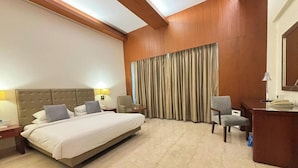 A hotel room with a large bed, a desk, a chair, and a large window with curtains. - The Hans Hotel New Delhi (New Delhi)
