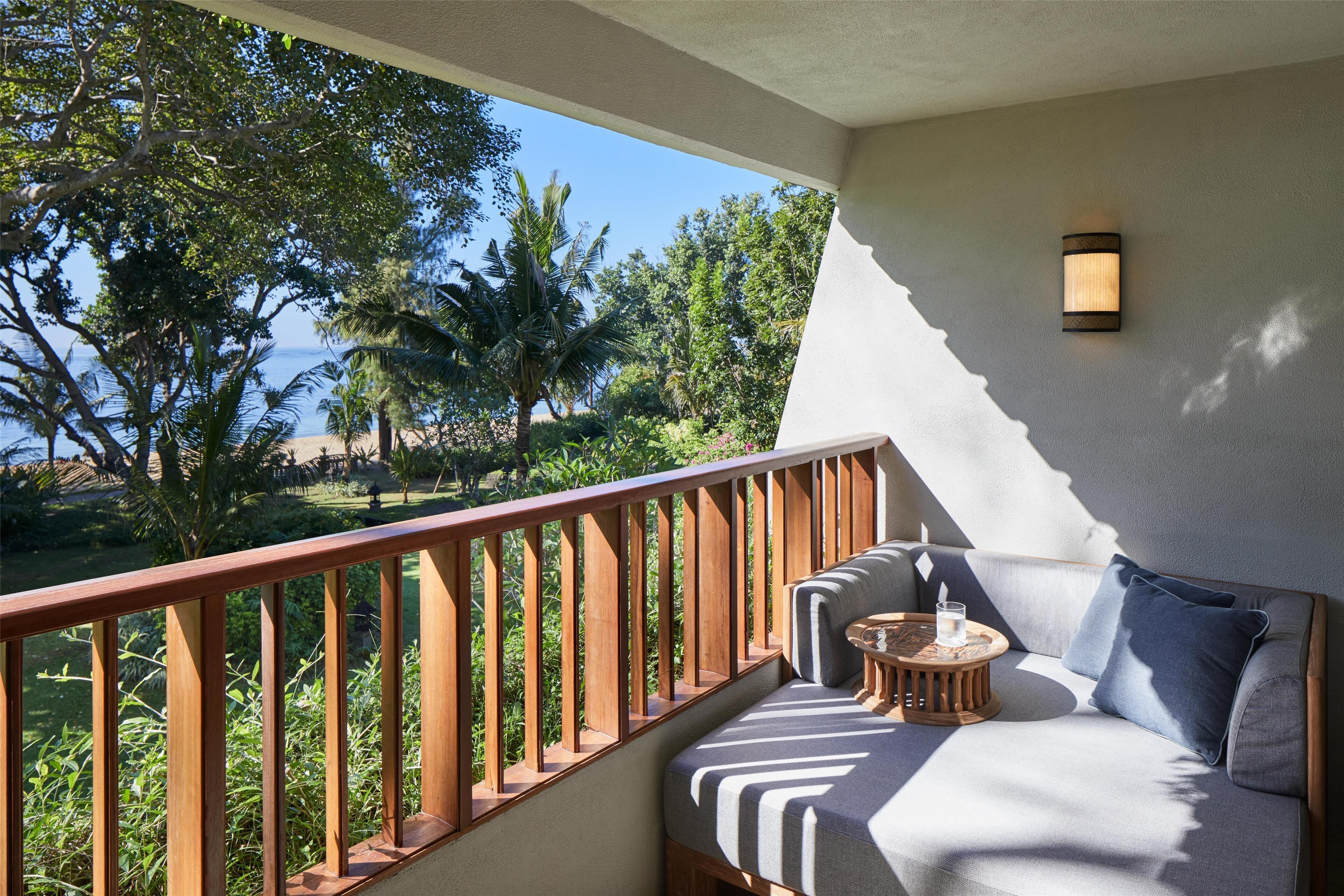 A balcony with a wooden railing, a cushioned seating area with a small round table, and a wall-mounted light fixture.