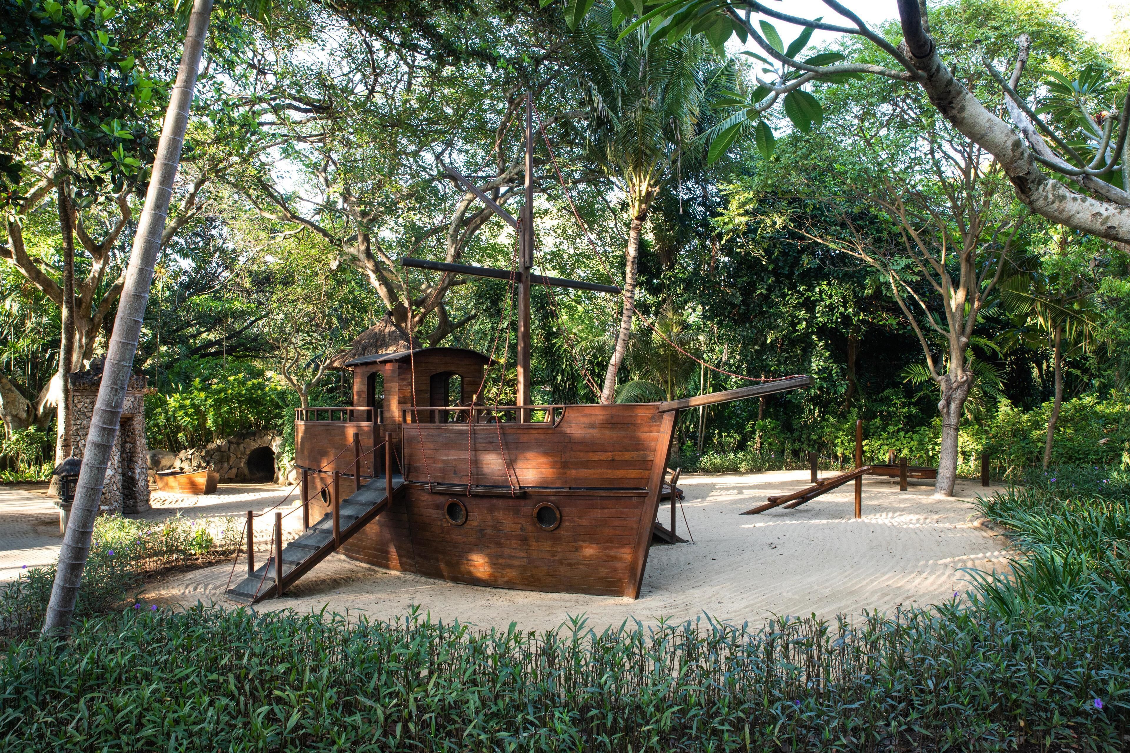 A wooden ship structure surrounded by lush greenery and trees.