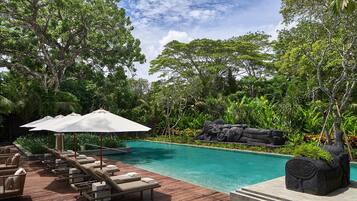 A pool area with lounge chairs and umbrellas, surrounded by lush greenery and a stone sculpture.