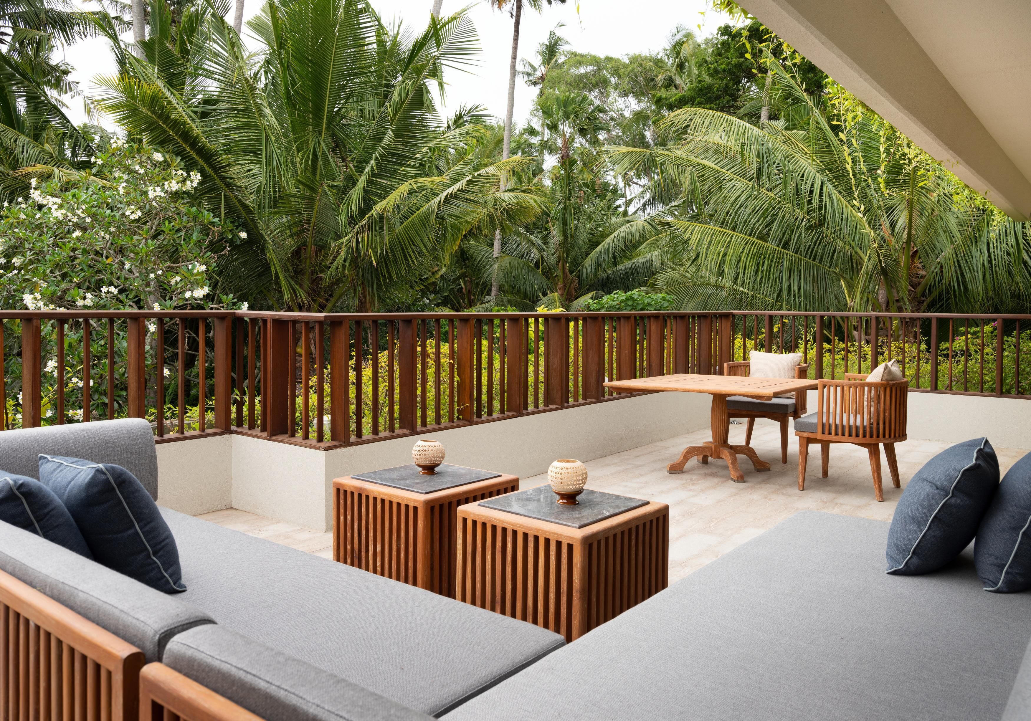 A balcony with a wooden table and chairs, a sofa, and a railing.