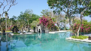 A clear pool surrounded by lush greenery and pink flowers.