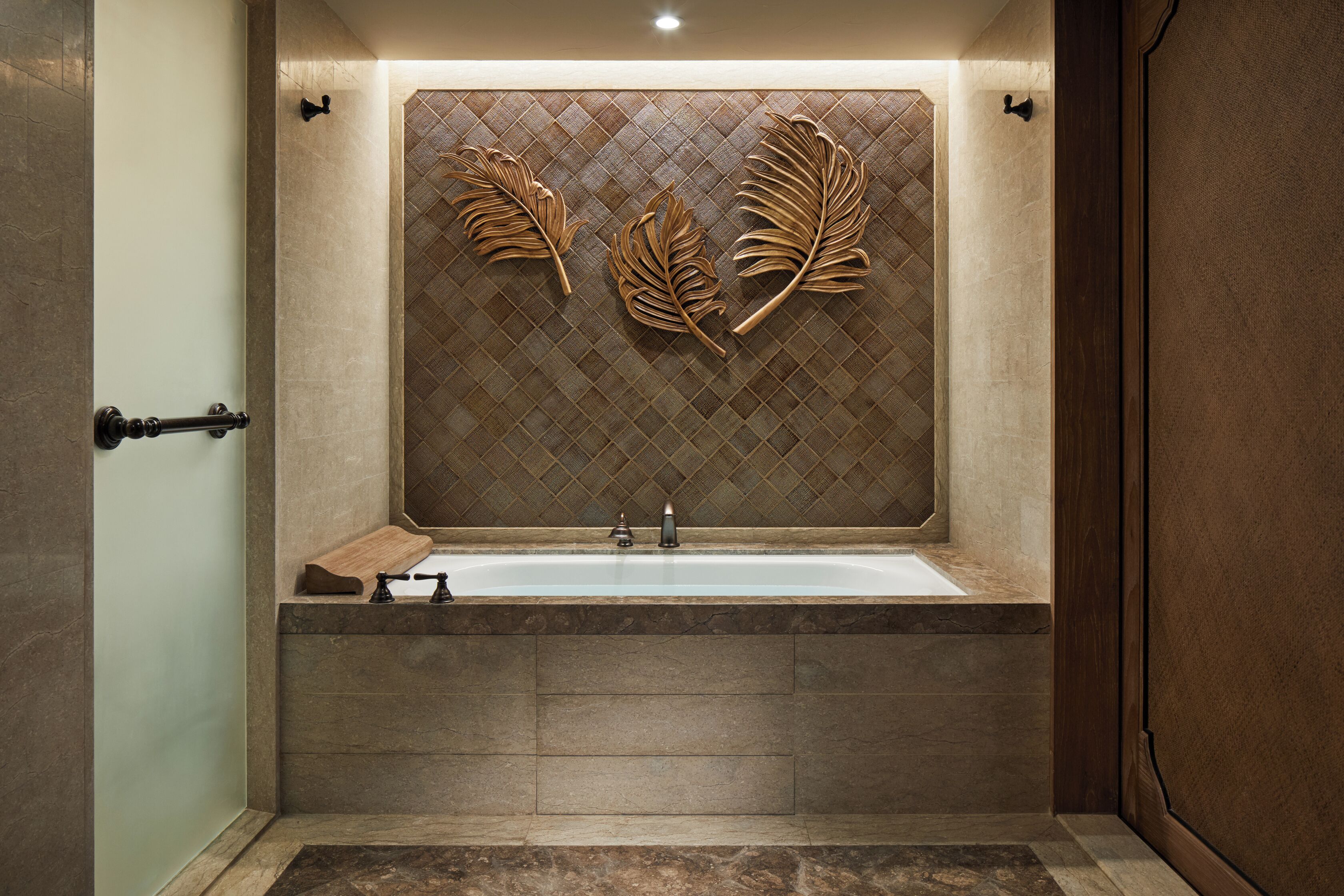 A modern bathroom with a large bathtub, a wooden bench, and decorative leaf wall art.