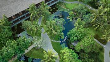 Vista aérea de un jardín exuberante con un estanque central, palmeras y un edificio con techo de paja.