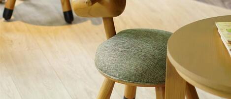 A wooden chair with a green seat and black accents, positioned on a light wooden floor.