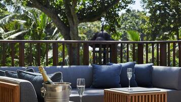 Un espacio al aire libre con una mesa de madera, un sofá acolchado y un árbol grande al fondo.