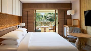 Habitación de hotel con cama, una mesita, dos sillas, televisor y balcón con vistas a palmeras.
