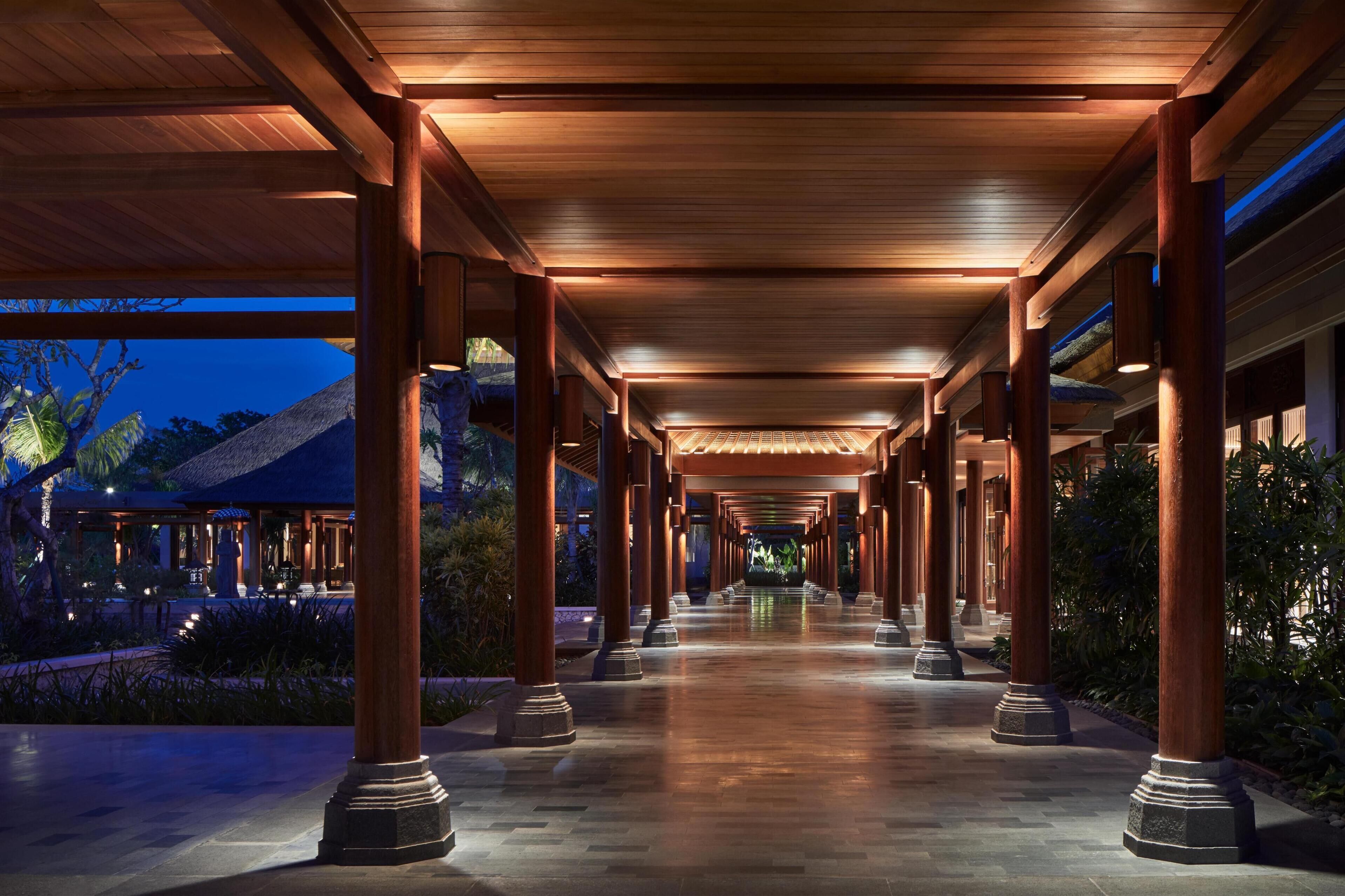 A covered walkway with wooden columns and a thatched-roof building in the background.