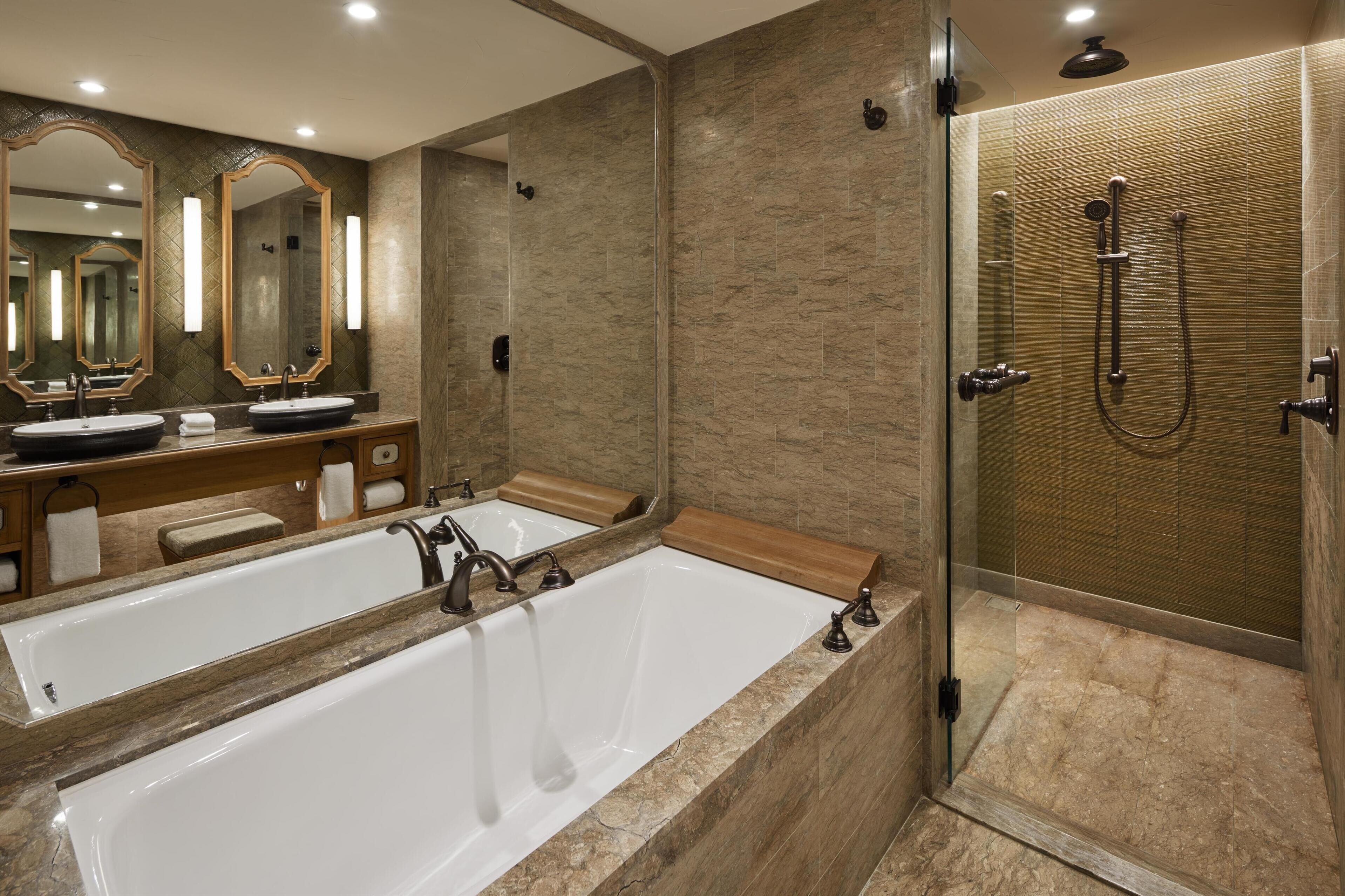 A modern bathroom with a large bathtub, two sinks, and a walk-in shower.