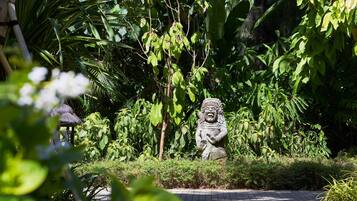 A garden with a stone statue, lush greenery, and a paved walkway.