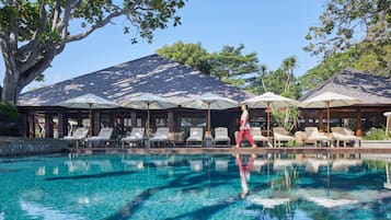 A pool area with lounge chairs and umbrellas, surrounded by trees and a building with a sloped roof.