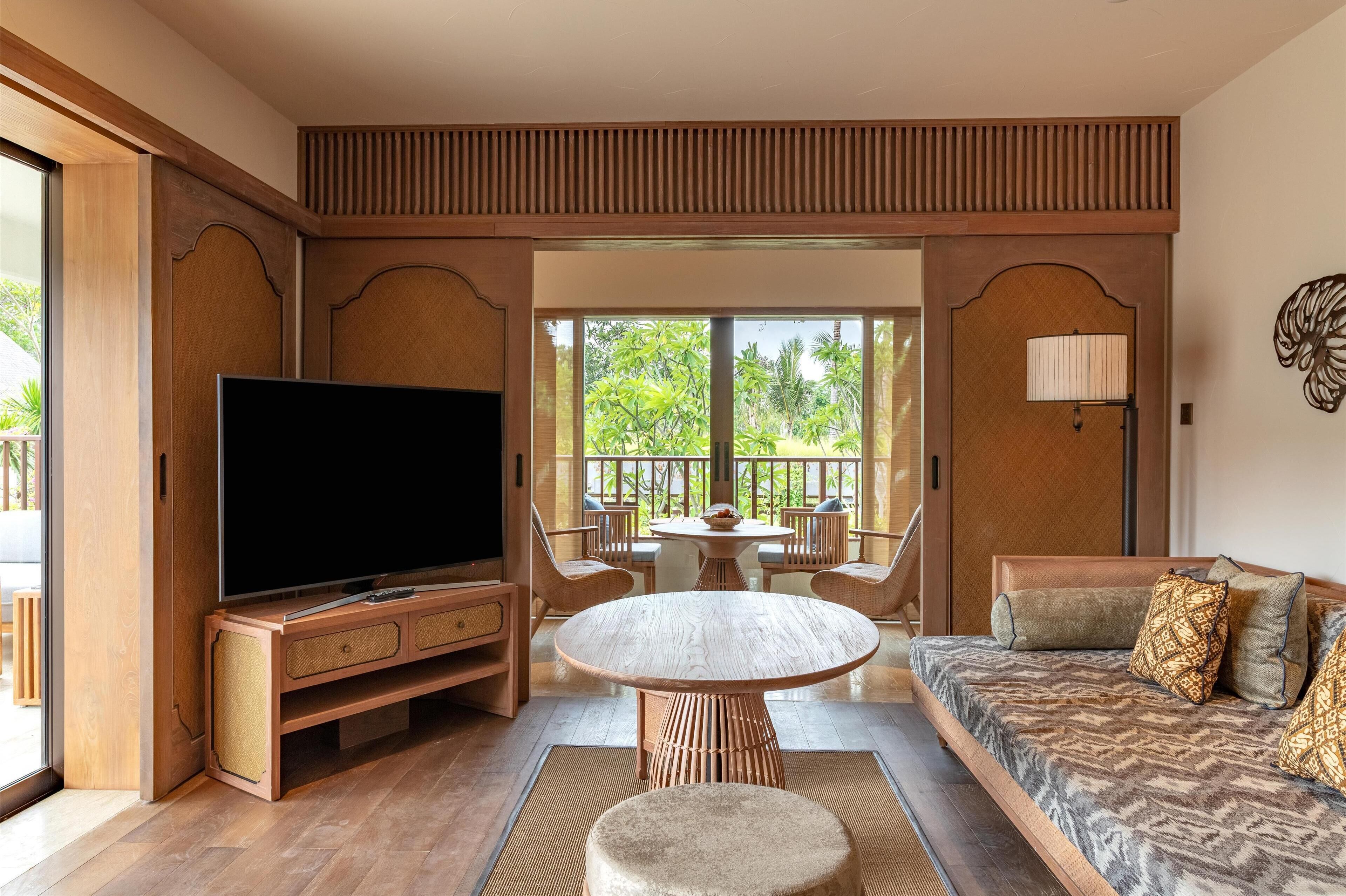 Una sala de estar moderna con un televisor de pantalla plana, una mesa redonda de madera y un sofá con cojines estampados.