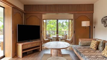 Un salon moderne avec un téléviseur à écran plat, une table ronde en bois et un canapé agrémenté de coussins à motifs.