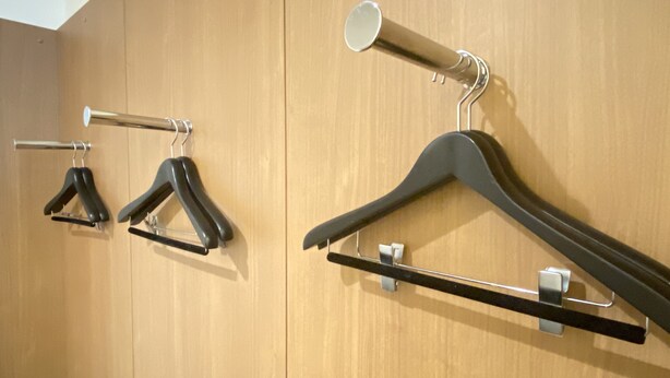 A wooden wardrobe with two black hangers and a coat rack with a coat and a mirror.
