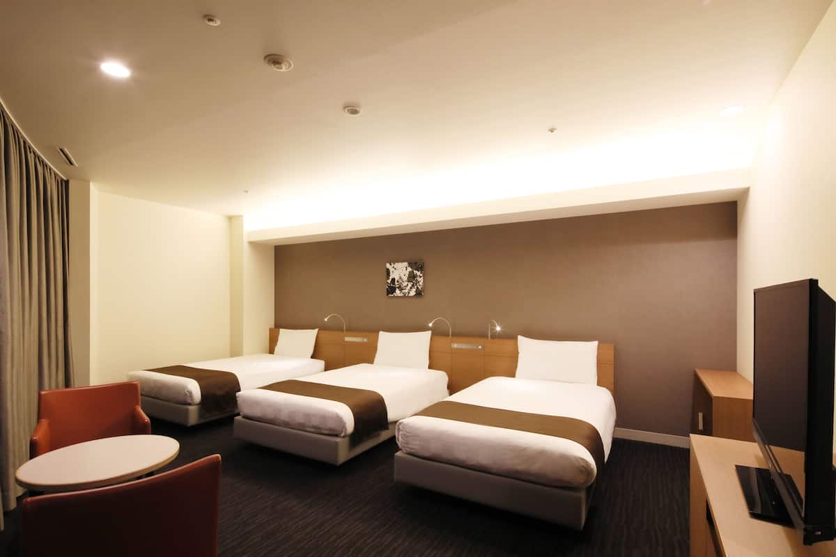 A hotel room with two beds, a TV, a desk, and a chair.