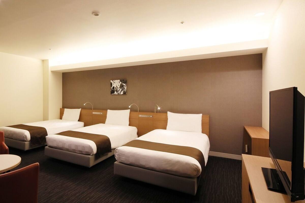 A hotel room with two beds, a desk, a chair, and a television.
