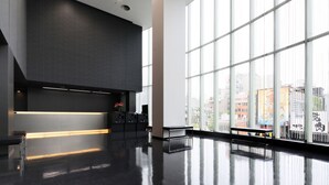 A spacious lobby with a modern design, featuring a reception desk, a bench, and large windows offering a view of the cityscape. - Hiroshima Tokyu REI Hotel (Hiroshima)