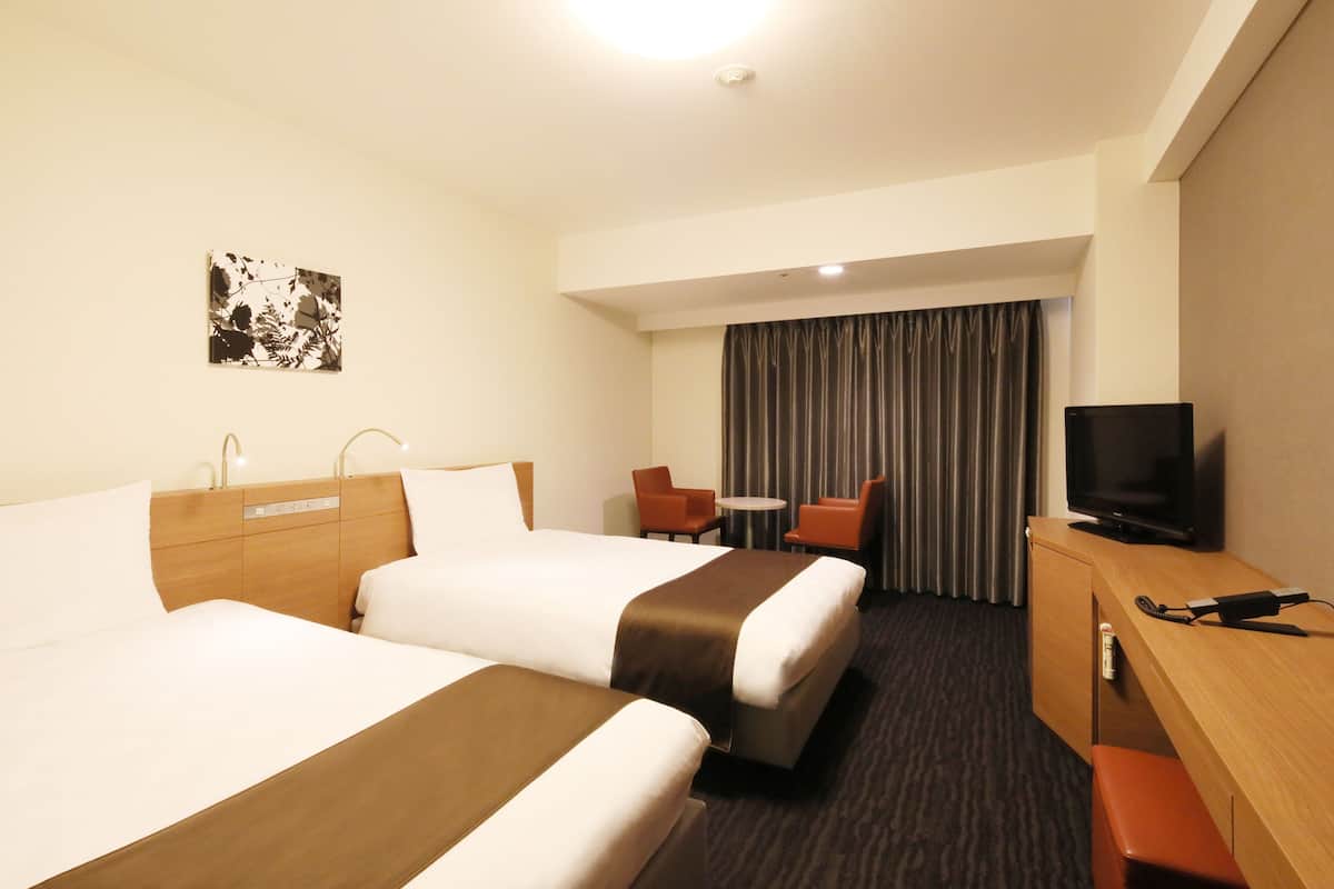A hotel room with two beds, a desk with a television, a small table, and a chair.