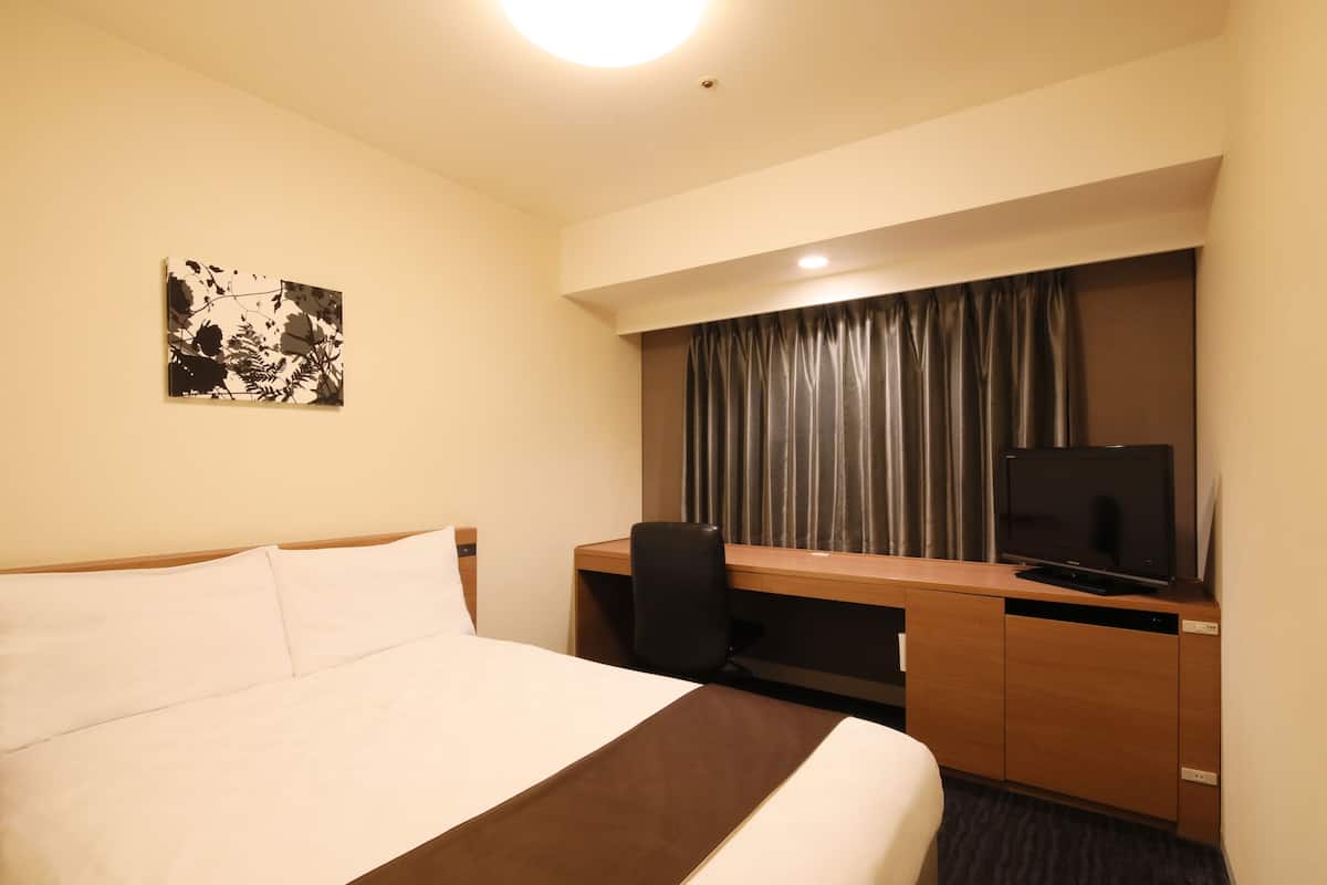 A hotel room with a bed, a desk, a television, and a window with curtains.
