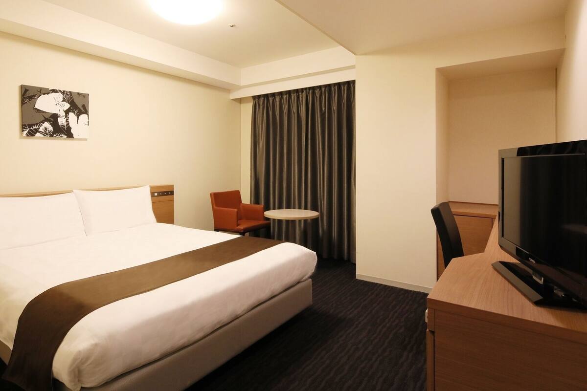 A hotel room with a bed, a television, a chair, a small table, and a painting on the wall.