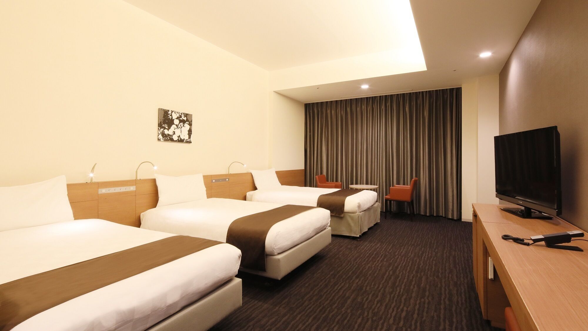 Habitación de hotel con dos camas, televisor, escritorio y cortina.