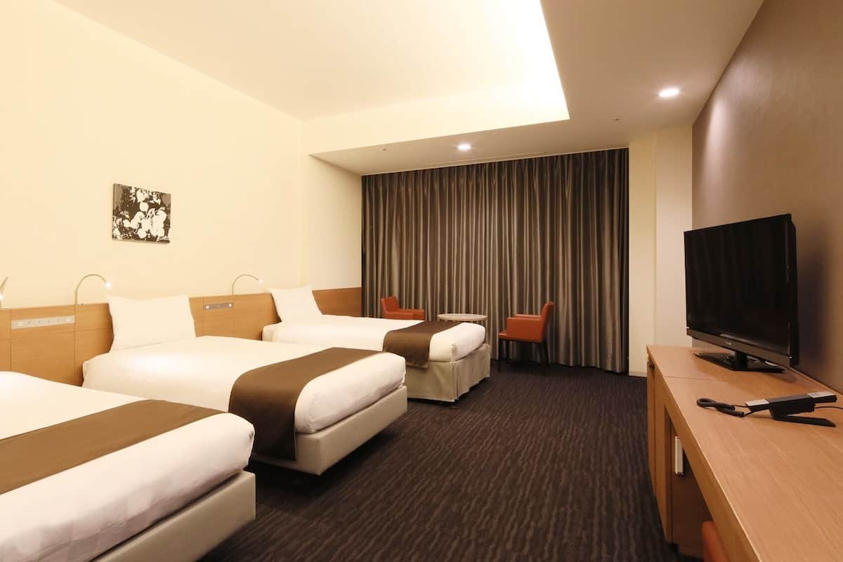 A hotel room with two beds, a TV, a desk, and a curtain.