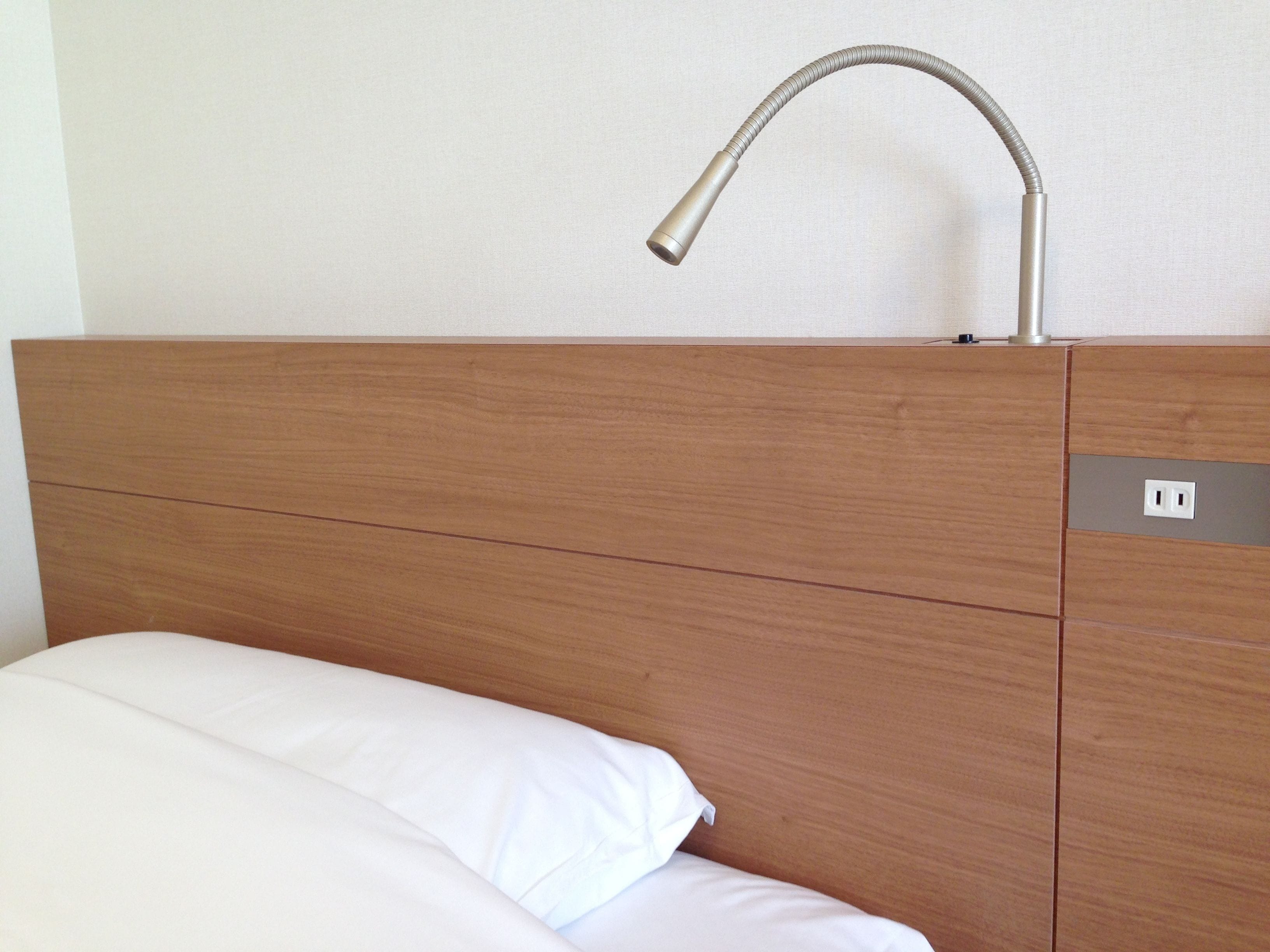 Una cama con ropa de cama blanca, cabecera de madera y un grifo moderno encima.