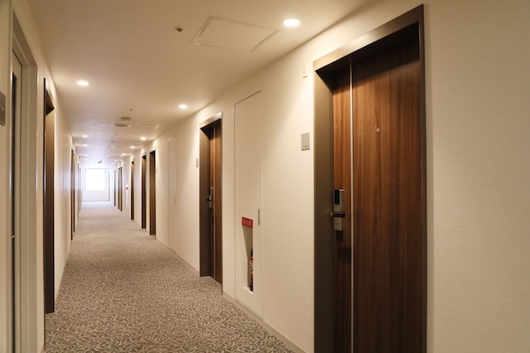 Pasillo de hotel con pisos alfombrados, puertas de madera e iluminación empotrada.