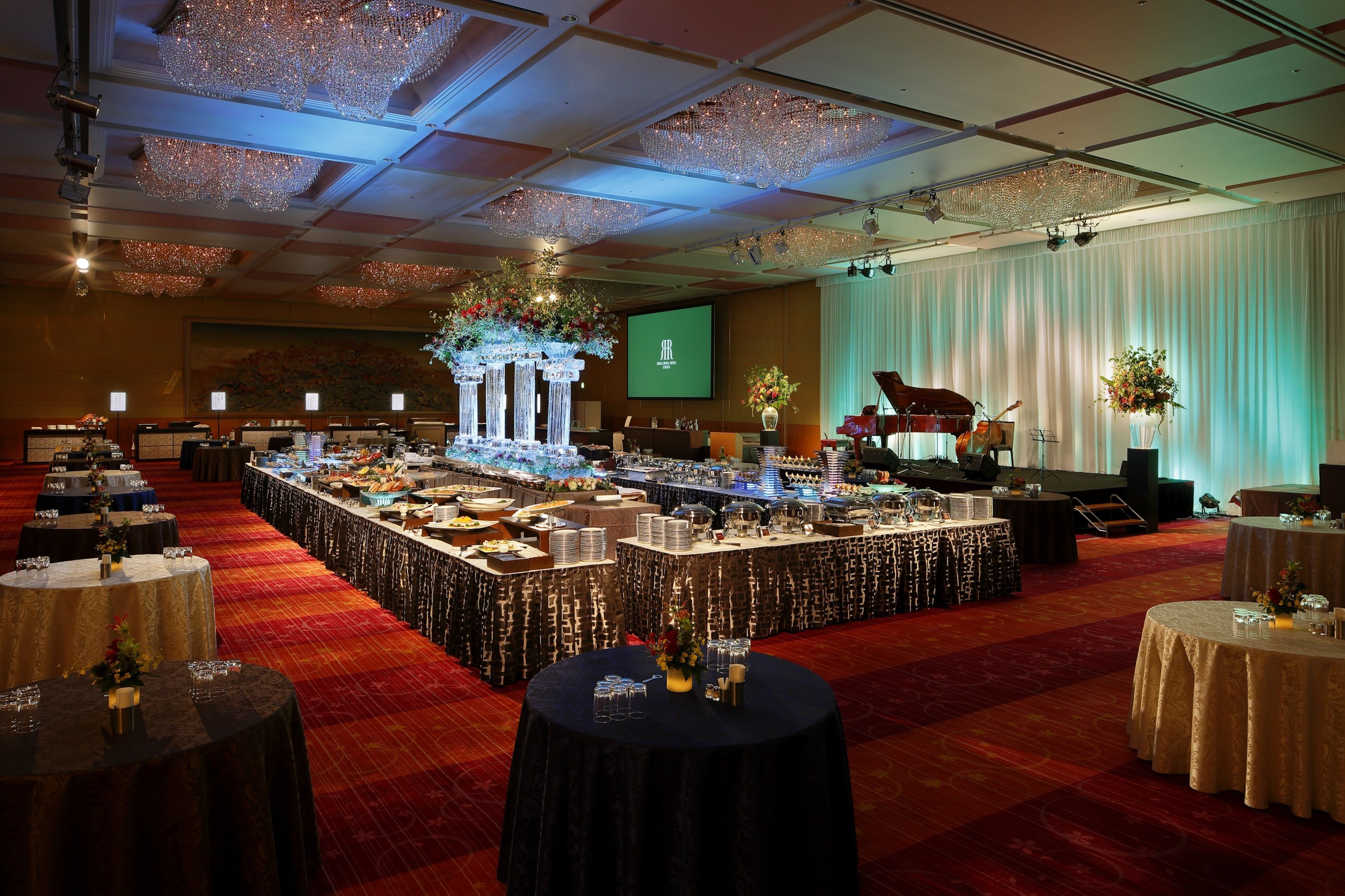 A banquet hall with a long table for dining, a stage with musical instruments, and a screen displaying a logo.