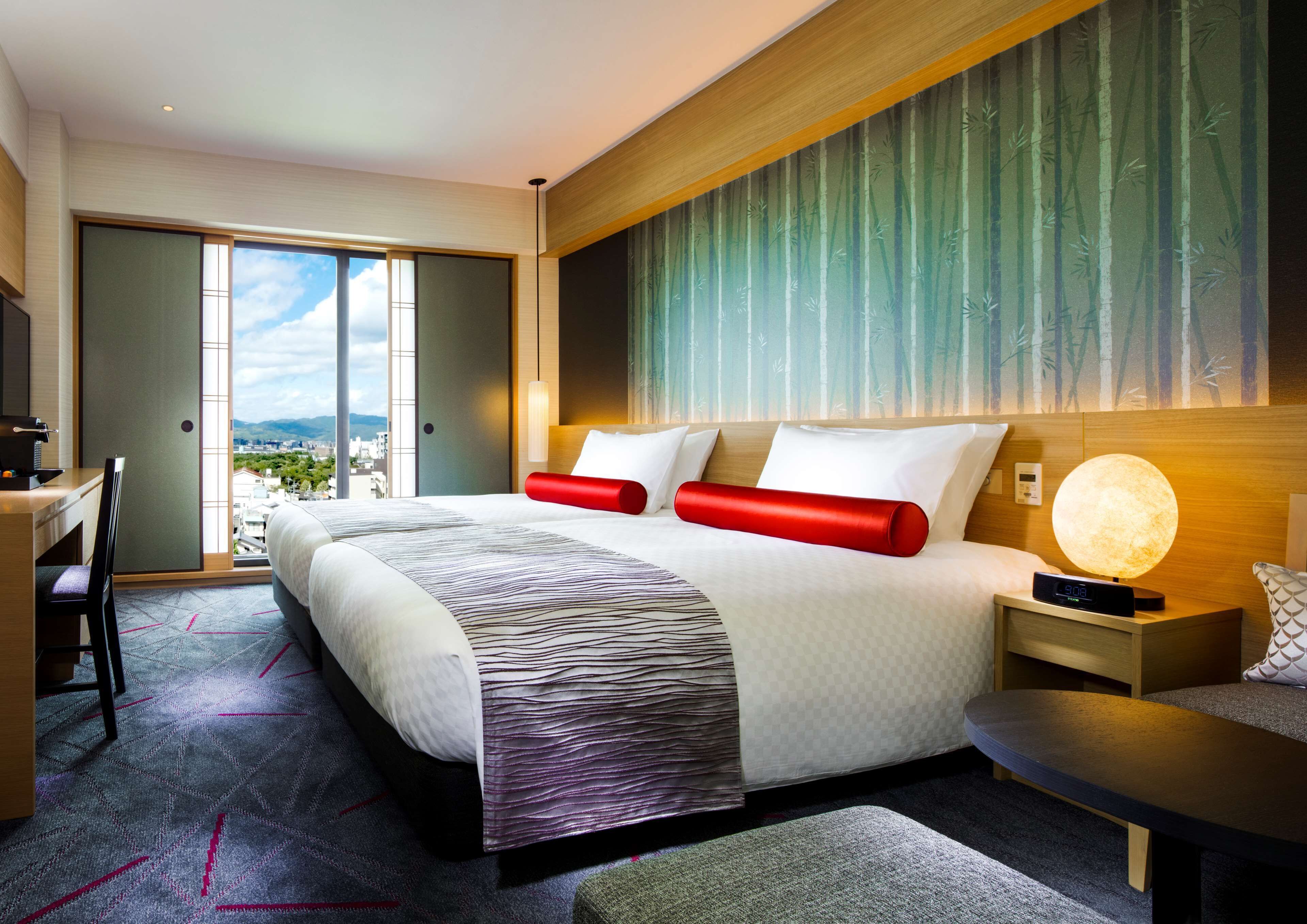 A modern hotel room with a large bed, a desk, and a view of the city.