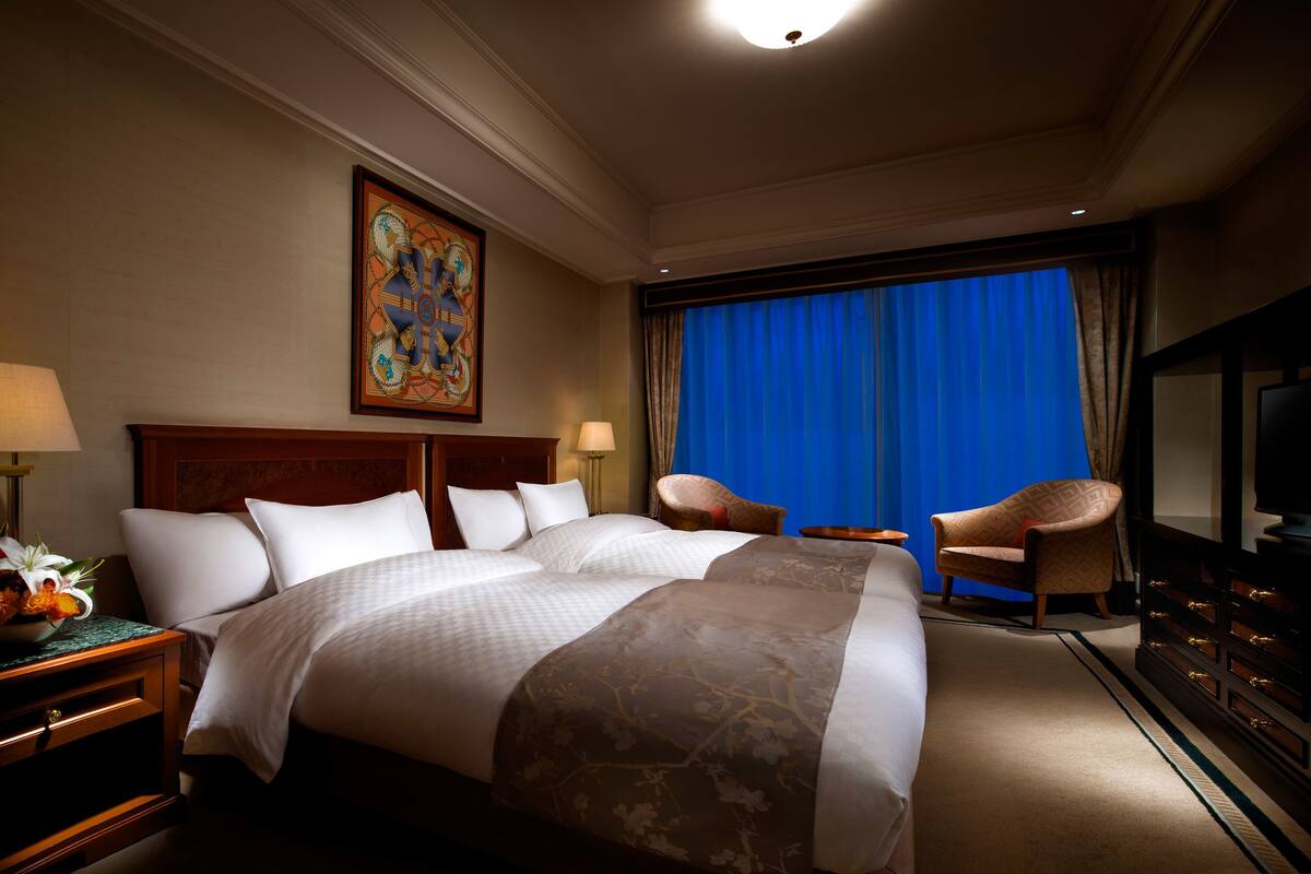Une chambre d’hôtel avec un grand lit, deux fauteuils, un téléviseur et un tableau au mur.